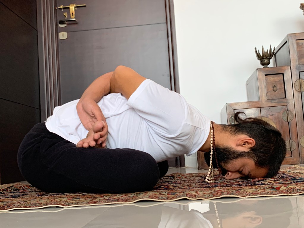 Hatha Yoga teacher Ayush performing Yogamudra Asana (forward bending of the spine) in variation Baddha Padmasana (locked lotus pose).