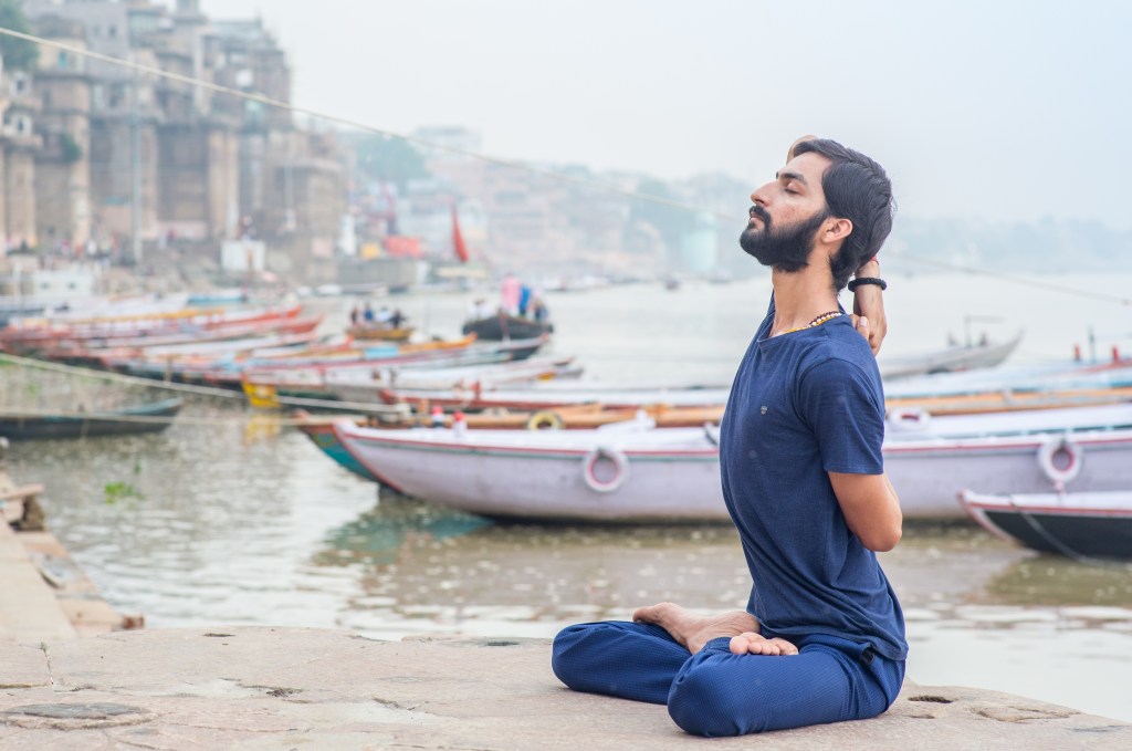 Hatha Yoga teacher Ayush performing Gomukhasana (Cow Face Pose) in Varanasi bank of the river (Ganges).