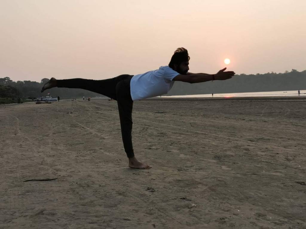 Hatha Yoga teacher Ayush performing Virabhadrasana III (Warrior 3 Pose) powerful standing posture in a beach  with Sunset. 
