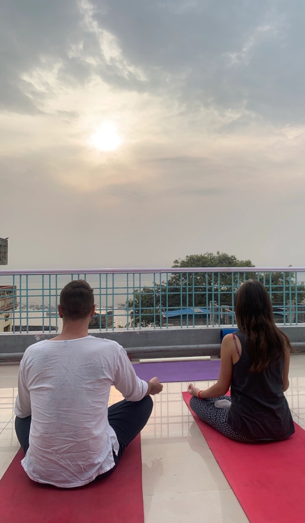 Yoga teacher Ayush students performing Padmasana overlooking sunrise with Ganga view.